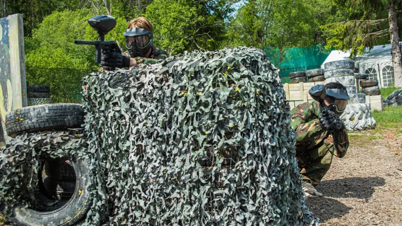 Spillere bak kamuflasjedekning på paintballbanen